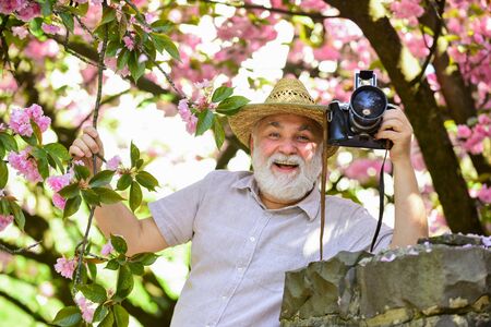 Senior man hold professional camera. Retirement travel. Enjoying free time. Travel and tourism. Capturing beauty. Happy grandfather. Spring holidays. Travel photo. Photographer in blooming gardenの写真素材
