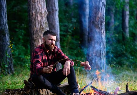 Man, hipster, hiker roast sausages on stick on bonfire