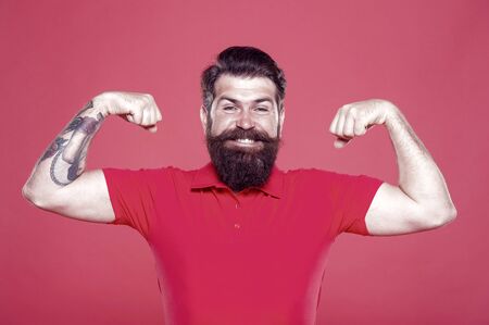 Mens power. Happy hipster fix arms red background. Bearded man show muscle power. Power training. Physical strength and power. Fitness and sport. Building biceps and triceps, vintage filterの写真素材