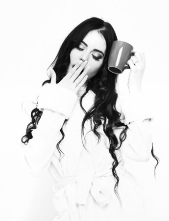 sexy yawning girl in beige velour bathrobe holding cupの写真素材