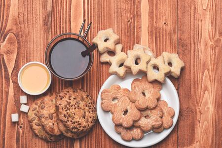 Hot beverage and pastry concept. Glass of black tea with various biscuits on plate near sugar cubes. Tea and cookies on wooden background. Composition of cup, honey and tiny gateau for tea timeの写真素材