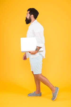 In trendy hipster style. Hipster hold computer yellow backgrounf. Bearded man with hipster beard in casual style. Hipster fashion. Modern life. Using new computing technologiesの写真素材