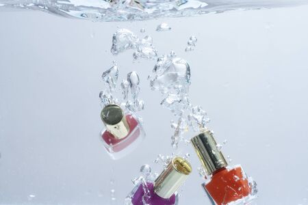 Nail polish fall into pure, transparent water. Beauty and care concept. Nail polish bottles under water with trail of transparent bubbles, white background.の写真素材
