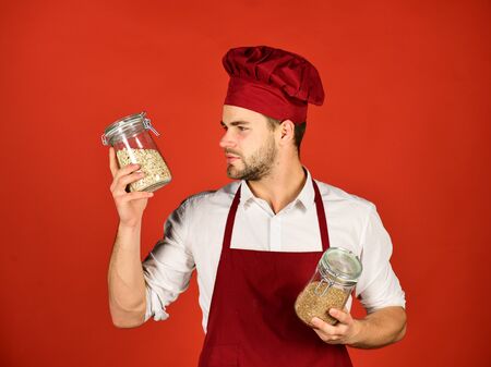 Chef in burgundy uniform holds jars with porridge.