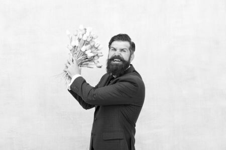 Angry bearded man with flowers. Celebrate spring. Date failure. Irritated annoyed aggressive bearded man with tulip bouquet. Disappointed concept. Failed date. Hate holidays. Womens day. March 8の写真素材