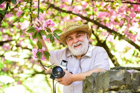 Retirement travel. Enjoying free time. Travel and tourism. Capturing beauty. Happy grandfather. Spring holidays. Travel photo. Photographer in blooming garden. Senior man hold professional cameraの写真素材