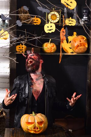 Devil or monster partying. Man wearing scary makeup with Halloween pumpkins and bats decor on...