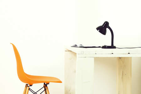 White wooden table with black lamp and open notepad, orange chair nearby isolated on white background. Workplace conception.の写真素材