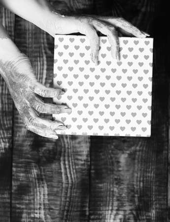 female hands smeared in golden paint or glister holding pink polka dots valentine present box on brown vintage studio backgroundの写真素材