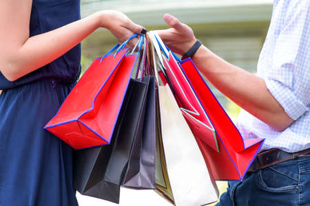 Colorful paper bags in hands of couple. Shopping and sales concept. Shopping bags in male and female hands. Handover of bags or gifts, close up.の写真素材