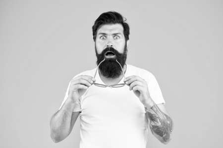 Super crazy surprise. Crazy hipster keep mouth open yellow background. Surprised bearded man hold glasses with crazy look. Barbershop. Fashion and style. Crazy and shockingの写真素材