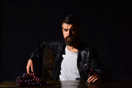 Degustator with confused face sits by wine bottle and grapes