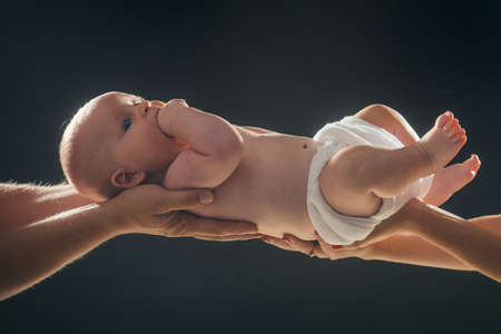 Newborn baby lies awake on parent hands. Newborn child with nappy in fathers and mothers hands. Infant held by hands of parents isolated on black background. Birth, fathers day, parentship concept.の写真素材