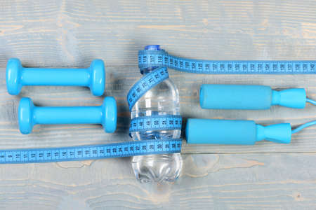 Tools for healthy and active lifestyle on wooden vintage background. Water, jump rope and barbells,...