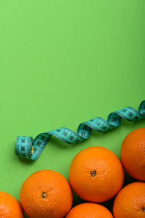Oranges near twisted measuring tape on green background, top view. Pattern made of orange fruits near tape measure in cyan blue color. Athletics and weight loss concept. Sports and healthy lifestyleの写真素材