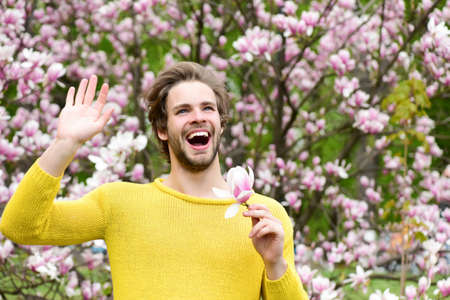 Happy man holding magnolia flower in park with blossoming treesの写真素材