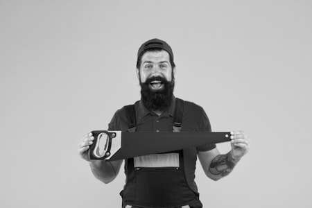 Gardener lumberjack equipment. Tools shop. Sharp blade of saw. Dangerous job. Feeling manly. Carpenter with saw in hands. Masculinity concept. Handsome smiling man happy with saw yellow backgroundの写真素材