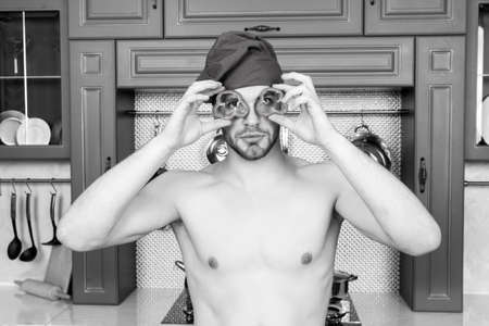 Man with red pepper slices like glasses. Cook in chef hat with  torso have fun kitchen. Vegetarian menu and healthy diet. Food preparation and cooking recipes. Fun, humor and joy of cookingの写真素材