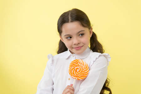 Girl happy face holds sweet lollipop ok gesture. She deserved candy. Girl likes sweet candy yellow background. Schoolgirl rewarded with candy for excellent marks. School achievement and sweet rewardの写真素材