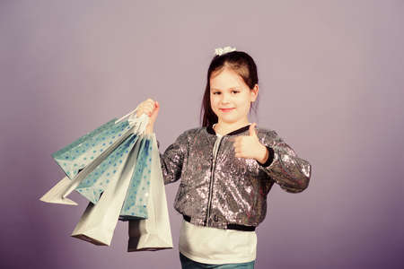 Girl with shopping bags violet background. Shopping and purchase. Black friday. Sale discount. Shopping day. Child hold bunch packages. Kids fashion. Surprise gift. Great stores. Great choicesの写真素材