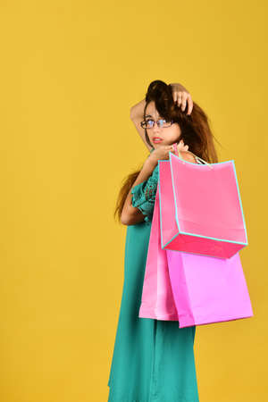 Girl stands on yellow background, holds pink shopping bagsの写真素材