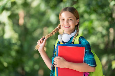 Girl in pigtails. Happy girl back to school. Little girl hold book bag natural outdoors. Shopping...
