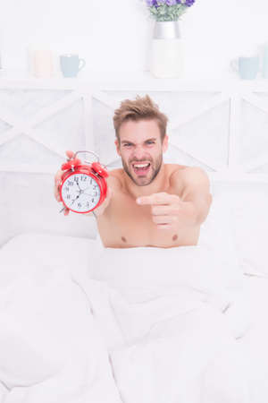 Stressful man point finger at clock face. Sexy guy slept through alarm clock.の写真素材
