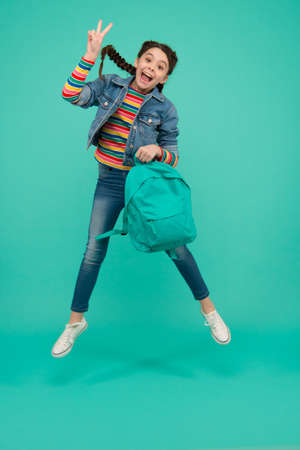 Adding a joy to your holidays. Happy girl jump blue background. Little child make victory sign in midair. School holidays. Leisure and free time. Summer vacation. Enjoying holidays. Fill thrill todayの写真素材