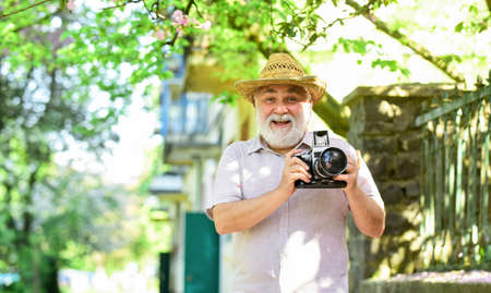 Enjoying free time. Travel and tourism. Capturing beauty. Senior man hold camera. Retirement travel. Spring holidays. Travel photo. Photographer in blooming garden. Walking his favorite streetの写真素材