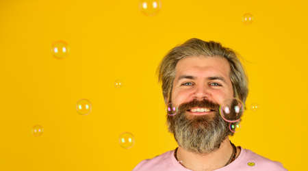 carefree man with bubble blower. happy hipster in playful mood. Fall into childhood. feeling childish and childlike. real happiness. april fools day. bearded man blowing soap bubbles. copy spaceの写真素材