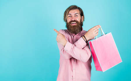 going to make payment in supermarket. best sale offer. happy bearded man with present pack. cheerful brutal hipster hold gift. paper shopping bag. birthday surprise at party. man with packageの写真素材