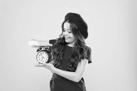 happy girl with long curly hair in beret. child with alarm clock. Timeless fashion. parisian child...