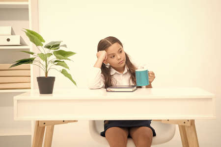 Use break to relax. Girl child hold mug while sit table white interior. Schoolgirl relaxing on break...