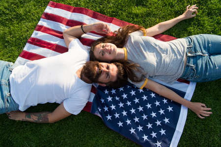 History of America. American patriotic people. American couple relaxing on USA flag outdoors....