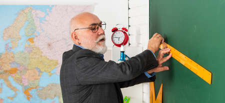 senior man teacher use ruler while drawing. tutor man in glasses draw with ruler on blackboard. back...