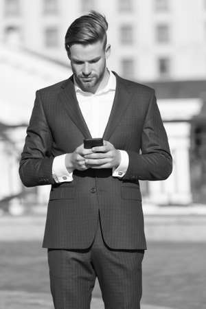 Message concept. Man in suit businessman takes advantages of modern mobile technologies. Man reads message mobile phone. Businessman serious face received important message, urban backgroundの写真素材