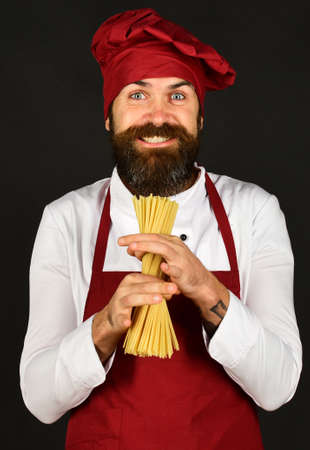 Cook with happy face in burgundy uniform holds dry pastaの写真素材