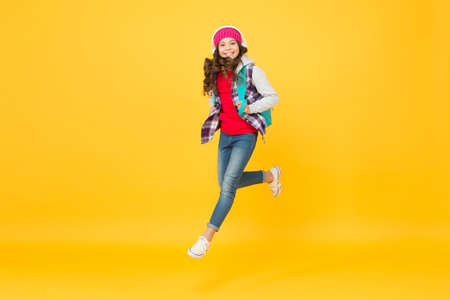 Life is a daring adventure. Happy child jump yellow background. Energetic girl wear backpack in...