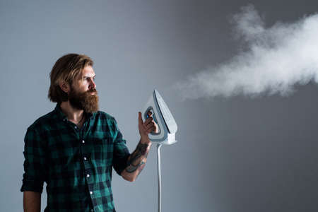 Professional Service. Man at home ironing clothes. house husband. Housekeeping. mature young man husband doing clothing ironing at home. hot and evaporation. modern life innovationの写真素材