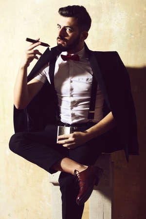 bearded man holding flask and smoking cigar with serious faceの写真素材