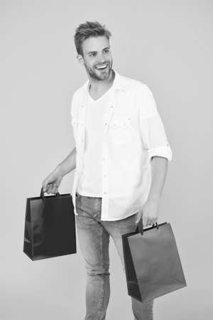 Handsome attractive man smiling while shopping. real shopaholic. buy gifts and presents online. guy doing shopping. shop assistant with packing bags. purchase delivery during quarantineの写真素材