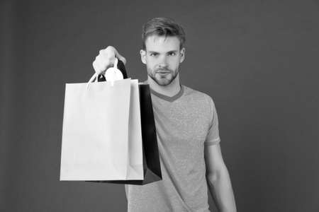 Macho with colorful paper bags on violet background. Man with shopping bags. Fashion shopper in...