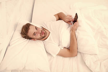 Provide deeper sleep analysis. Set up morning alarm. Apps that help monitor sleep. Man use mobile phone in bed. Waking up. Application analyzes stages of sleep and wakes you up at optimal timeの写真素材