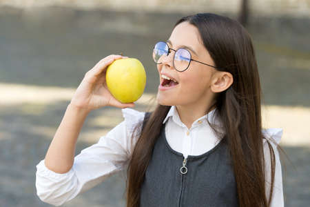Happy kid eat apple outdoors. School snack. Vitamin nutrition. Health education. Eating right carbs. Natural vitamin food. Energy diet. Give hoot, eat more fruitの写真素材