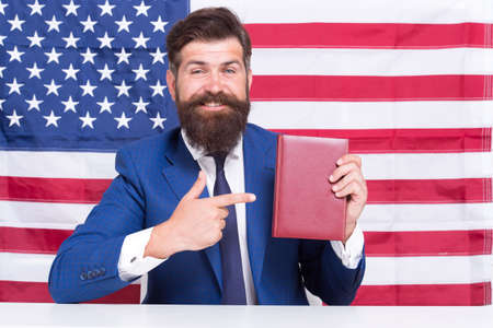 Turn attention. American businessman pointing index finger at book. Pointing at USA flag background. Pointing for advertising. English language school promotion. Pointing and promoting servicesの写真素材