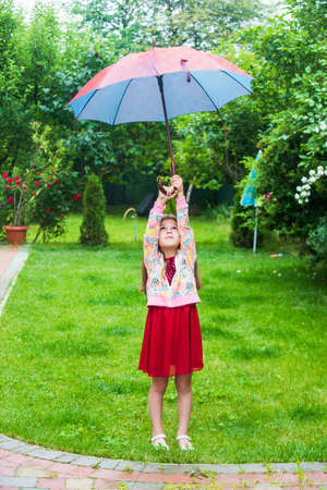 Small girl with umbrella in garden yard park, childhood happiness conceptの写真素材