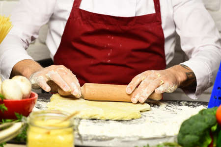 Male hands roll out dough on white brick wall background