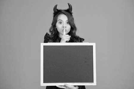 Shh. Halloween party. Halloween costumes designed after supernatural figures. Promoting event. Remember the ghoul times. Little girl cute horns Halloween advertisement. Child imp hold blackboardの写真素材