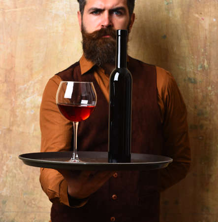 Waiter carrying tray with beverage. Glass and dark wine bottleの写真素材