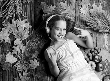 Fall music playlist. Song about fall. Enjoy music and relax. Girl lay fallen leaves wooden background. Music application for youth modern gadget. Child girl listen music headphones top viewの写真素材